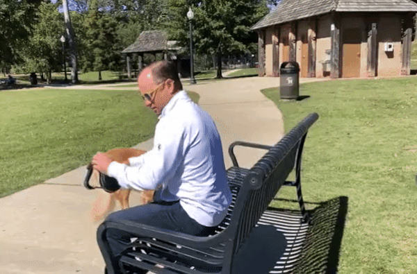 A dog owner clipping the Hitch Leash carabiner handle around a park bench in one motion