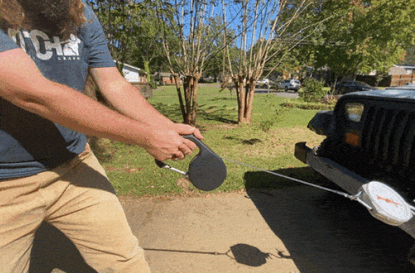 A Hitch Leash carabiner load-tested against a vehicle bumper with a hanging scale